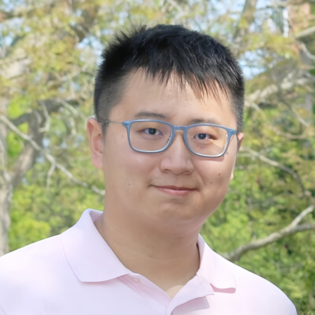 Portrait of Franklin Mingzhe Li, an Asian male with short black hair, wearing blue glasses and a light pink polo shirt, standing outdoors with trees in the background.