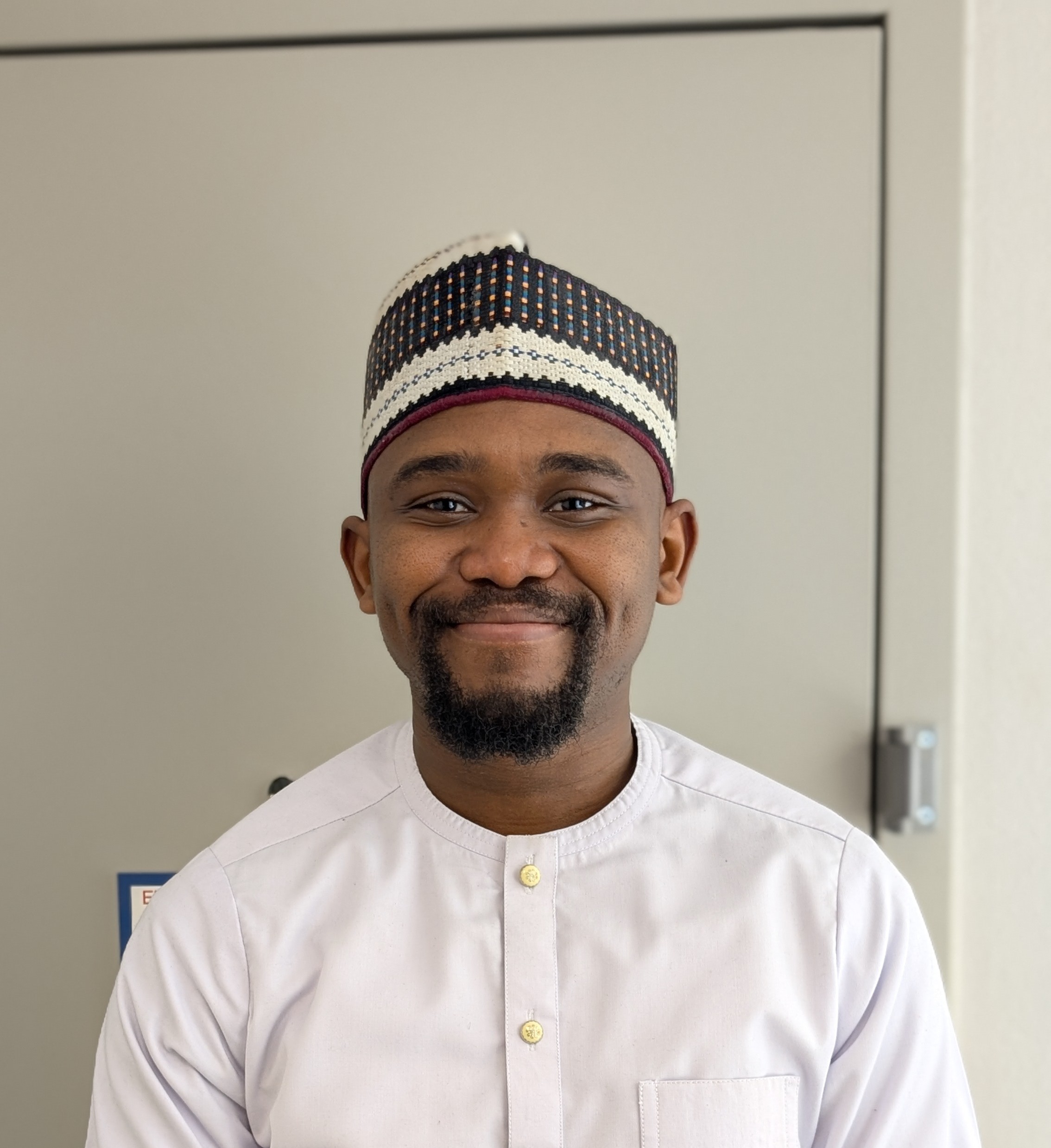 A headshot of Paul, an african man, smiling and wearing a light-colored shirt and a patterned cap.