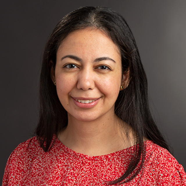 A picture of Yasmine, a woman smiling and wearing a red shirt.