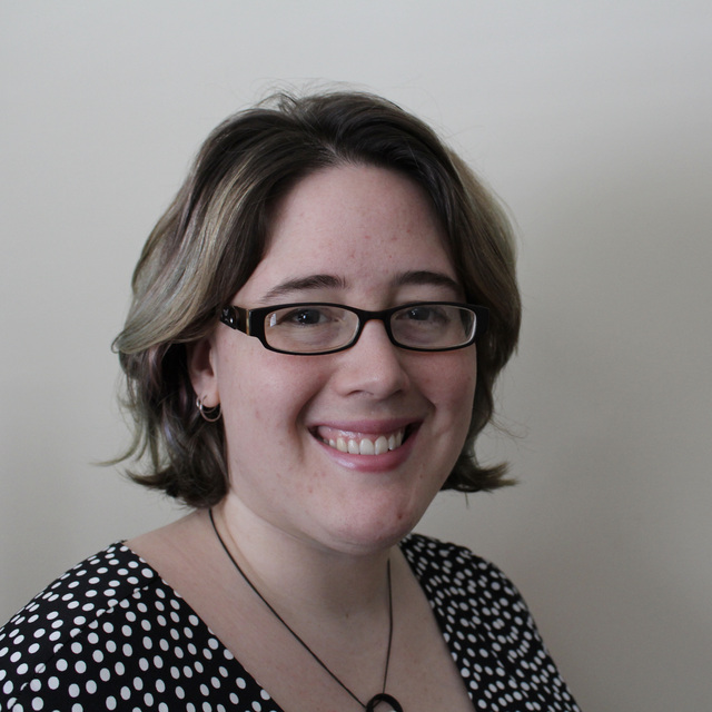 A picture of Elaine, a white woman with short brown hair and glasses and a polka-dot top, in front of a plain white background.